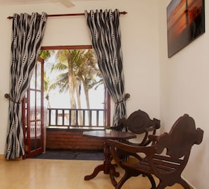 A room with a wooden table and chairs, a view of palm trees through an open door, and patterned curtains.