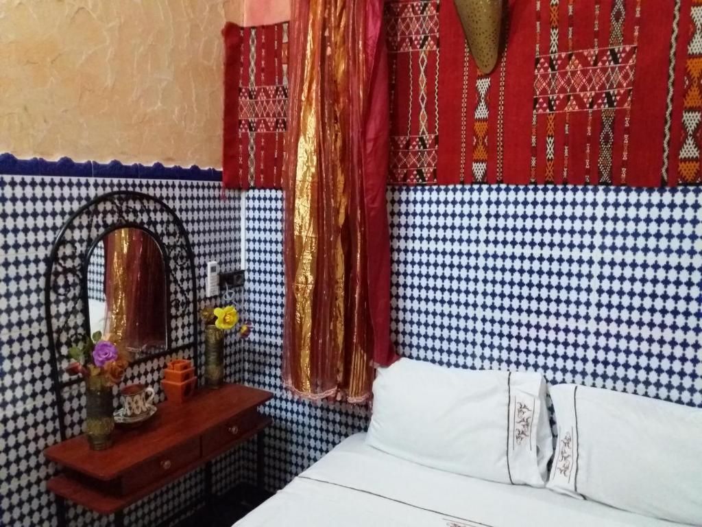 Un dormitorio con pared estampada, una cama con ropa blanca, una mesita de noche de madera con espejo y una cortina roja.