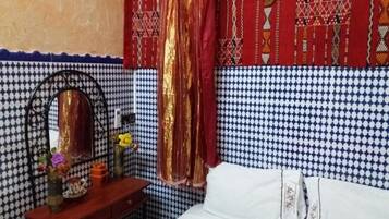 Un dormitorio con pared estampada, una cama con ropa blanca, una mesita de noche de madera con espejo y una cortina roja.
