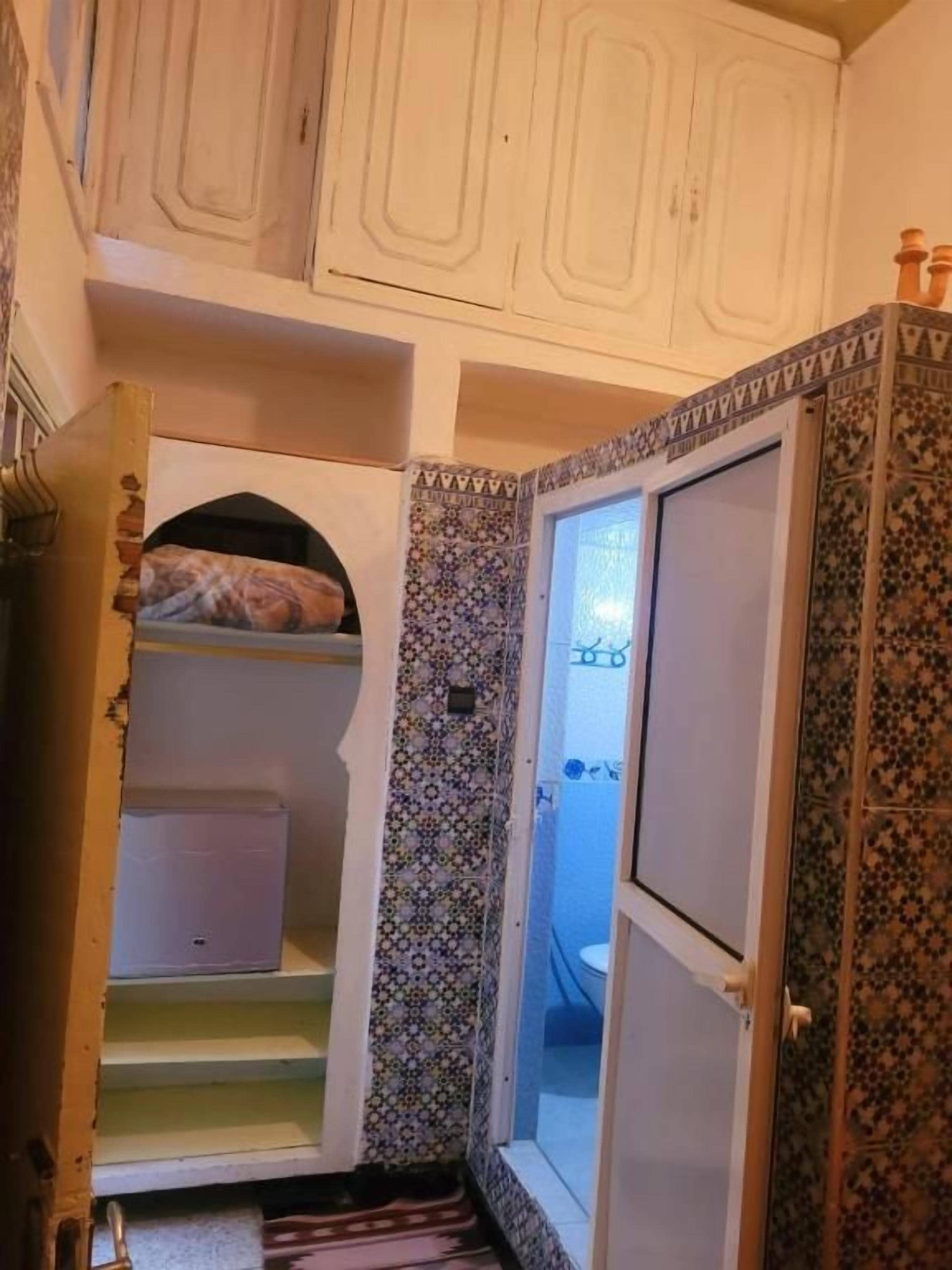 A narrow hallway with a patterned wall, a door leading to a bathroom, and a small shelf with a patterned item.