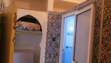 A narrow hallway with a patterned wall, a door leading to a bathroom, and a small shelf with a patterned item.