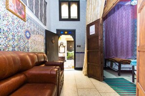 A narrow hallway with a leather sofa, a bed with a striped bedspread, and a patterned wall. - Dar Berrada ziat  (Fès)