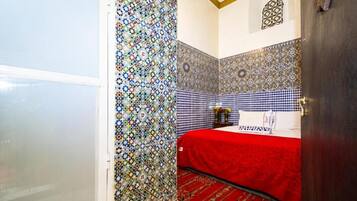 Quarto com cama, colcha vermelha, paredes estampadas e uma janela pequena.