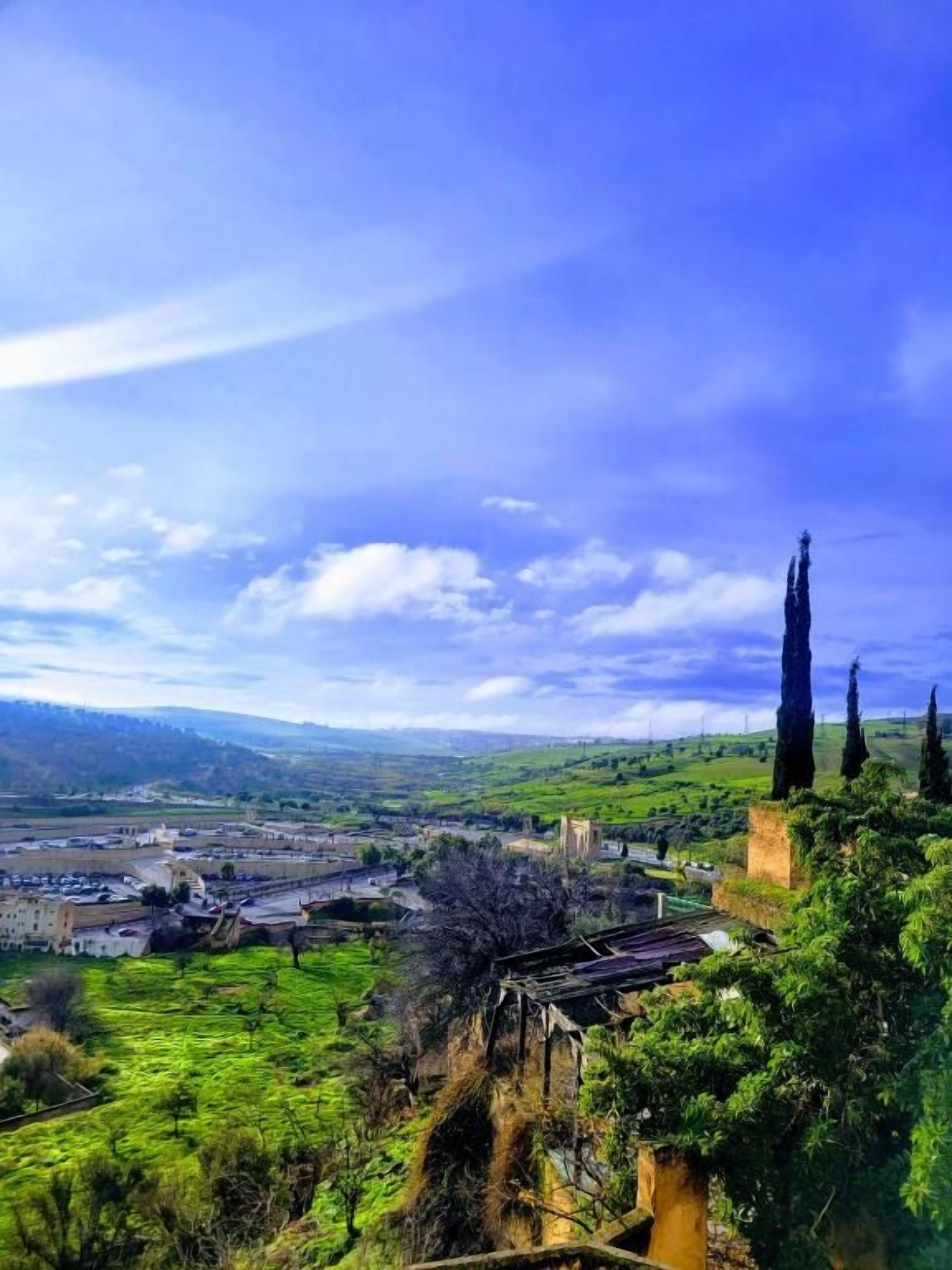 Une vue panoramique d’une ville avec une église imposante, des collines ondoyantes et un ciel dégagé.
