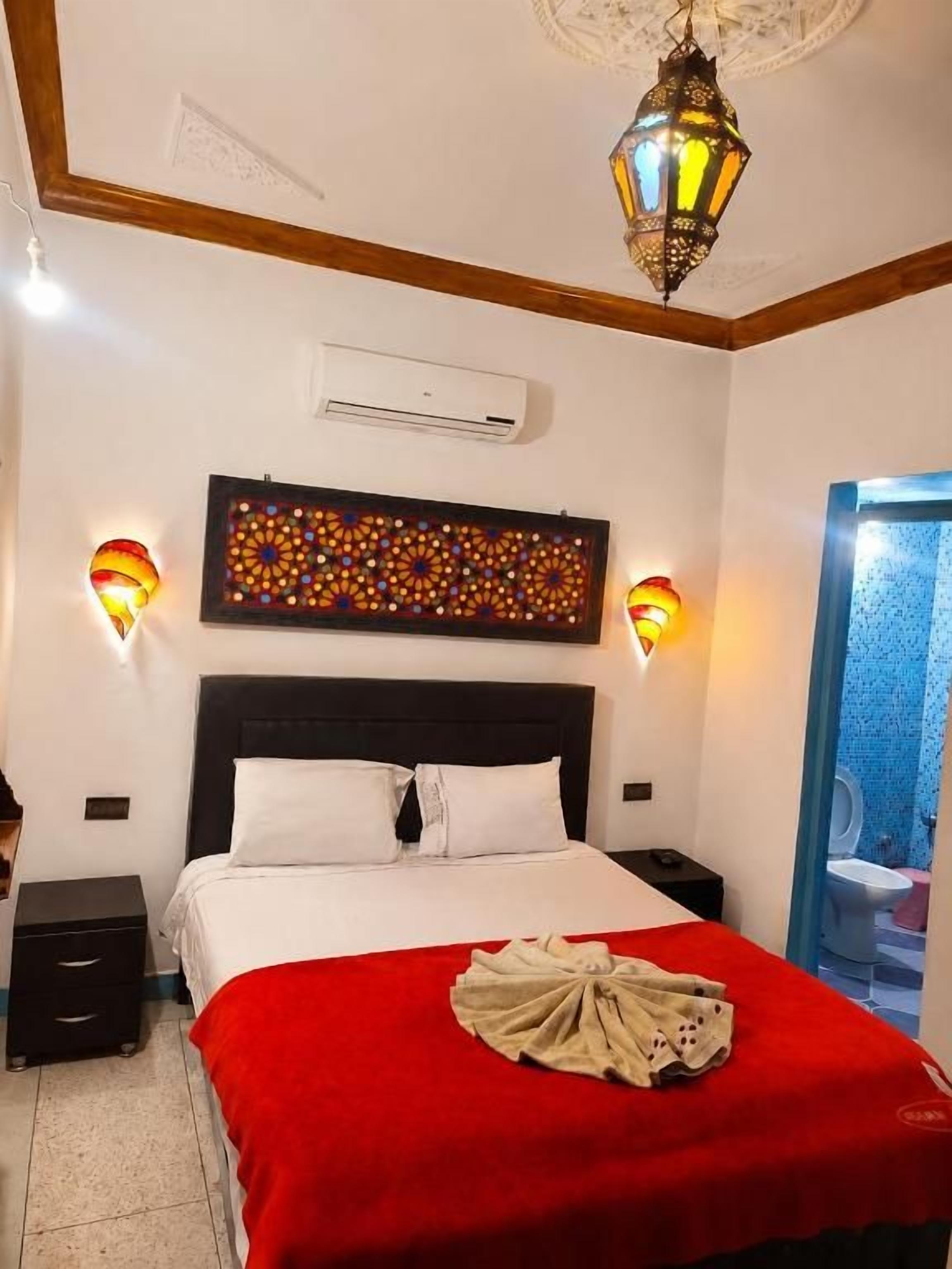 A hotel room with a bed, bedside lamps, a wall-mounted air conditioner, and a view of the outside.