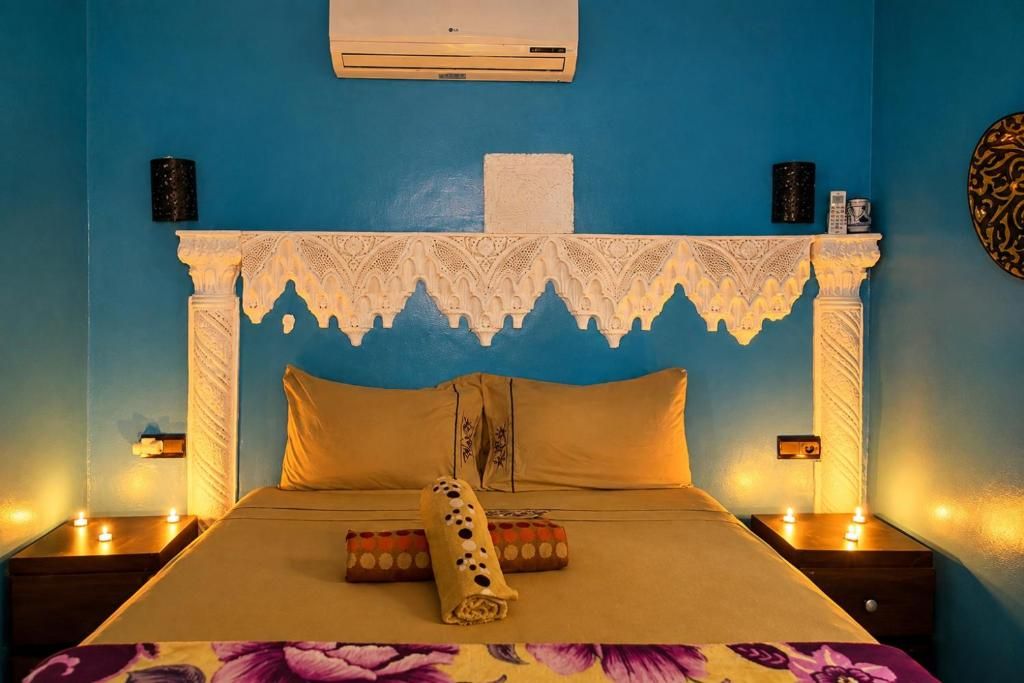 A room with a bed, a decorative headboard, bedside lamps, and a wall-mounted air conditioner.