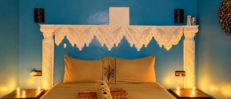 Una habitación con una cama, cabecera decorativa, lámparas de noche y aire acondicionado instalado en la pared.