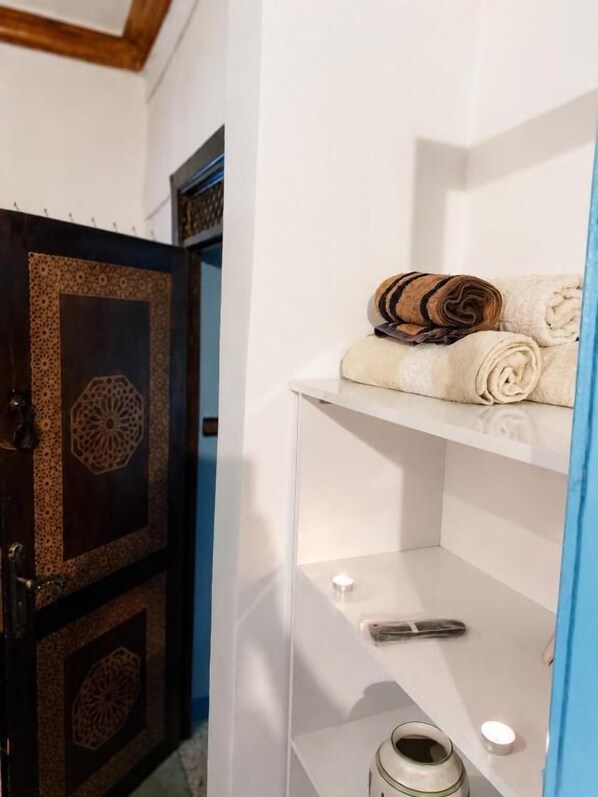 A bathroom with a towel rack holding rolled towels, a shelf with a bottle, and a decorative door. - Dar Berrada ziat  (Fès)