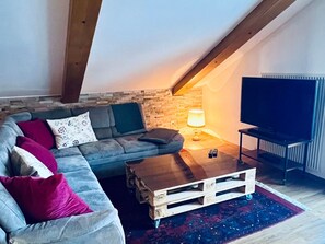 A loft-style living room with a sofa, a coffee table, a TV, and a stone wall. - Apartmenthaus Gauenpark (CharmingStay), (Flumserberg Tannenheim), by Interhome (Flumserberg Tannenheim)