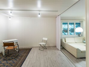 Ein Zimmer mit einem weißen Schreibtisch, einem Klappstuhl, einer Couch und einem gemusterten Teppich.