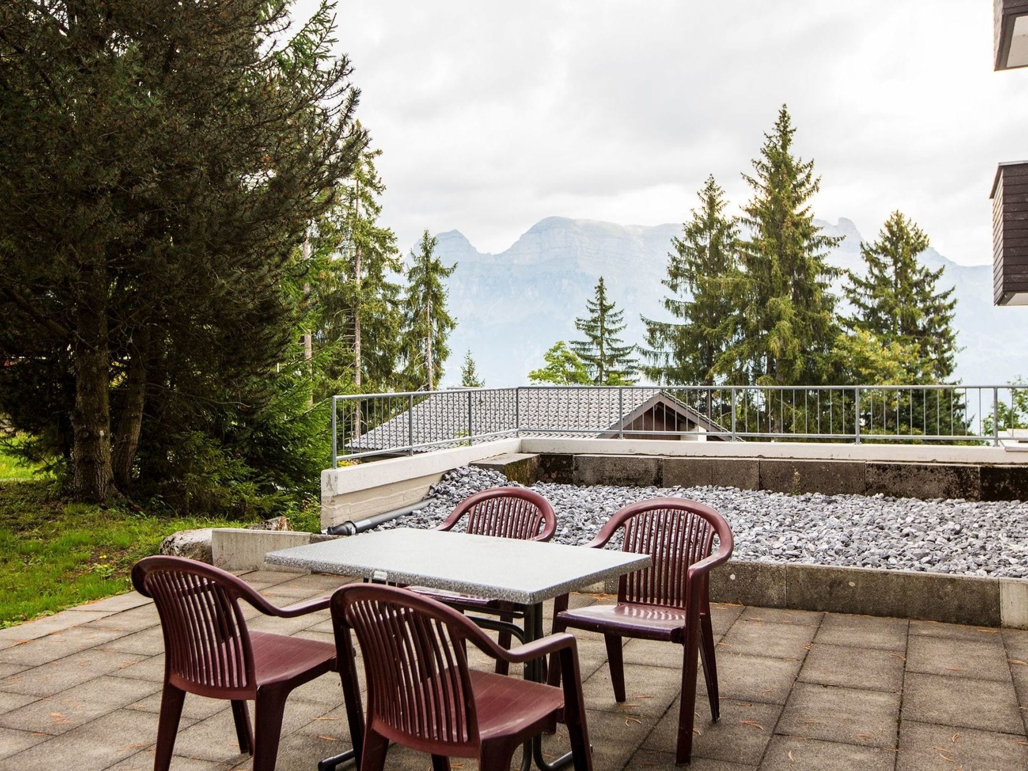 Un espace extérieur aménagé avec une table et des chaises, entouré d’une rambarde, offrant une vue sur un paysage montagneux.