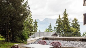 An outdoor seating area with a table and chairs, surrounded by a railing, overlooking a mountainous landscape. - Apartmenthaus Gauenpark (CharmingStay), (Flumserberg Tannenheim), by Interhome (Flumserberg Tannenheim)