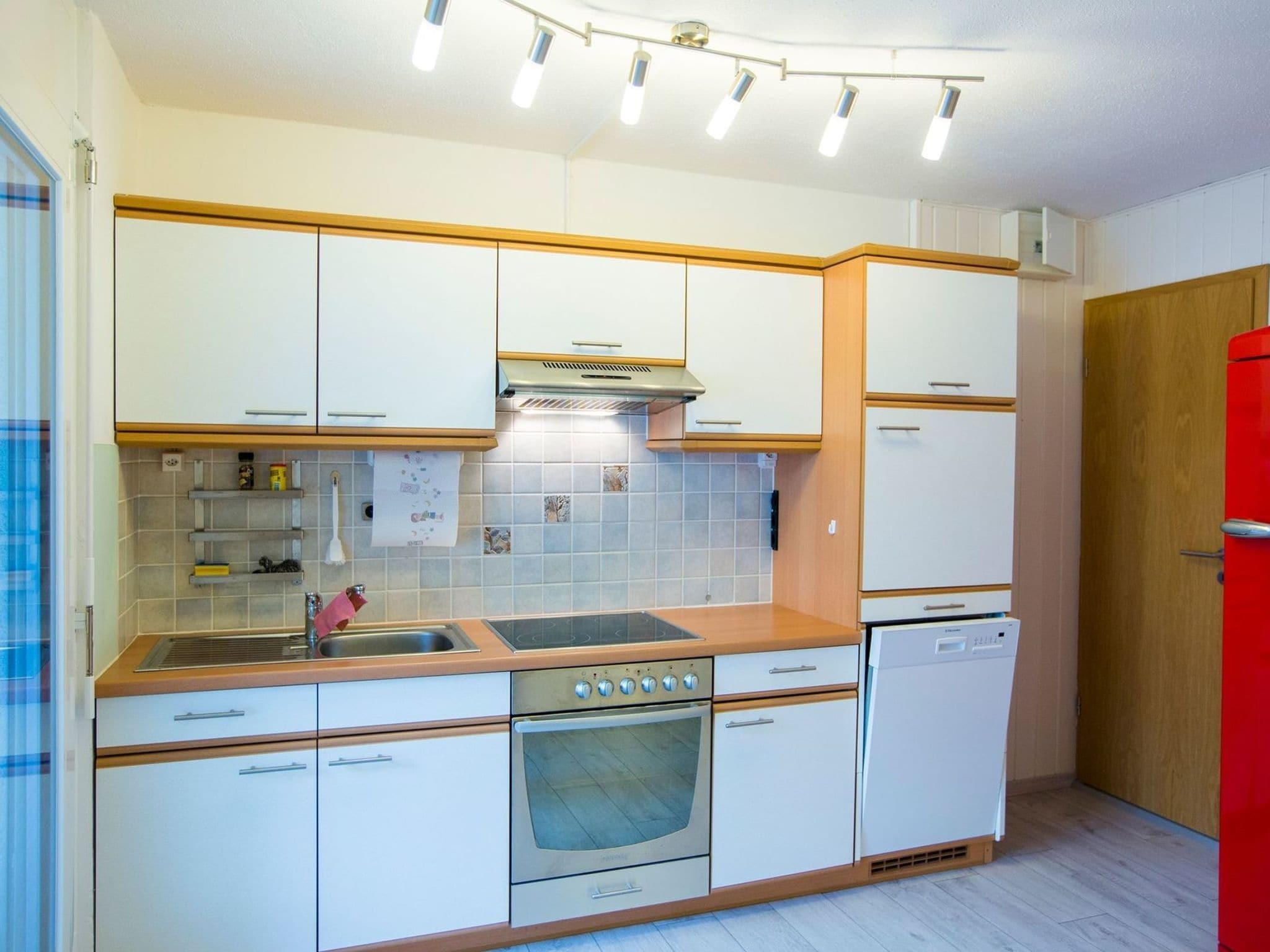 A compact kitchen with white cabinets, a stainless steel range, a built-in oven, and a red refrigerator.