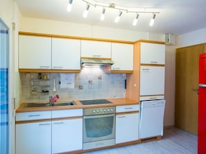 Eine kompakte Küche mit weißen Schränken, einem Edelstahlherd, einem eingebauten Ofen und einem roten Kühlschrank.