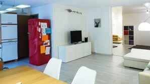 A modern kitchen with a red refrigerator, white cabinets, and a dining area with a wooden table and white chairs. - Apartmenthaus Gauenpark (CharmingStay), (Flumserberg Tannenheim), by Interhome (Flumserberg Tannenheim)