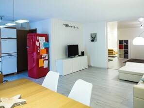 Una cucina moderna con un frigorifero rosso, mobili bianchi e un'area pranzo con un tavolo di legno e sedie bianche.