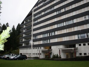 Un edificio a più piani con tetto piatto, ampie finestre e un'area di parcheggio con auto.