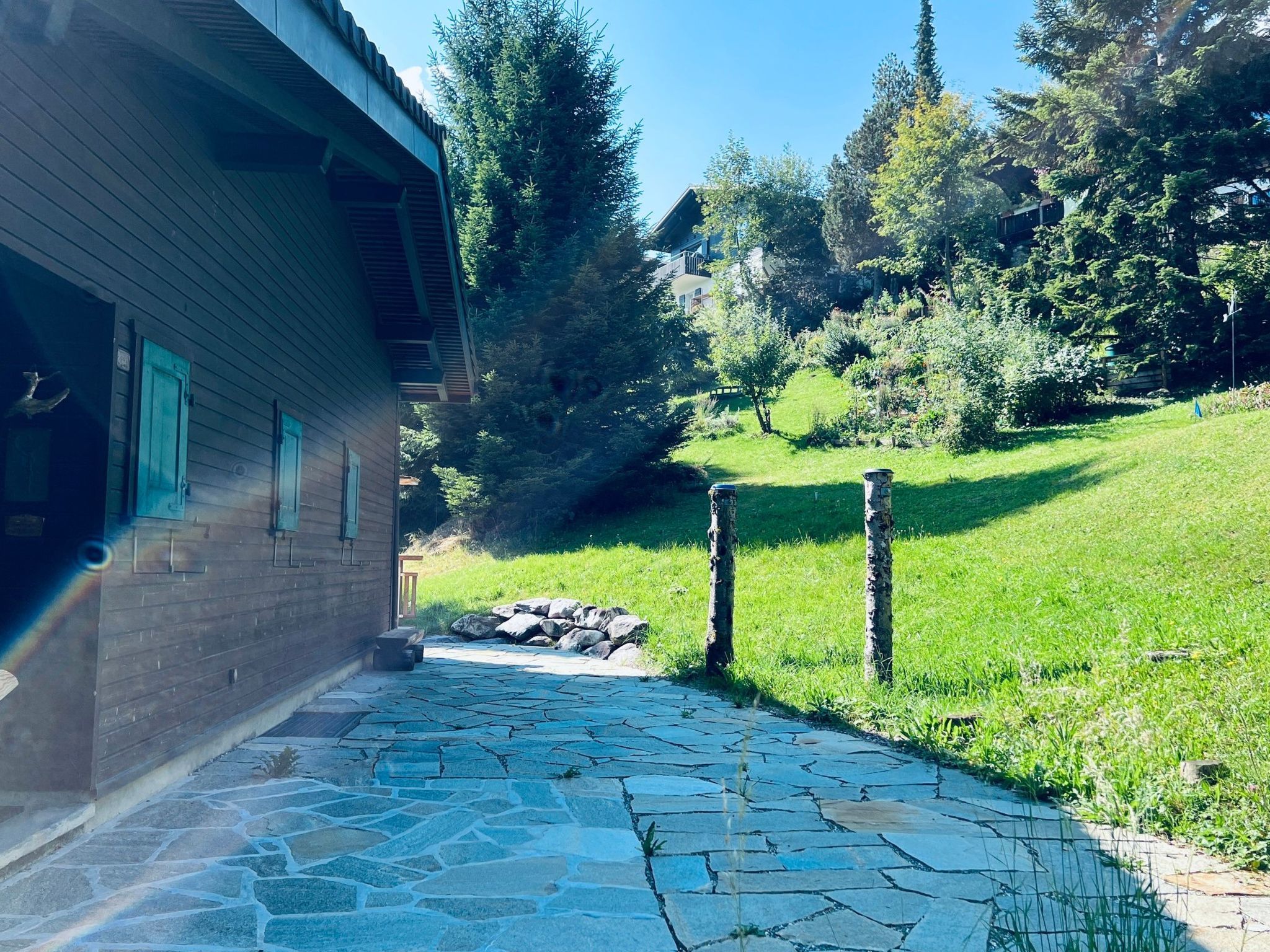 A stone pathway leading to a wooden building with a door, surrounded by lush greenery and trees.