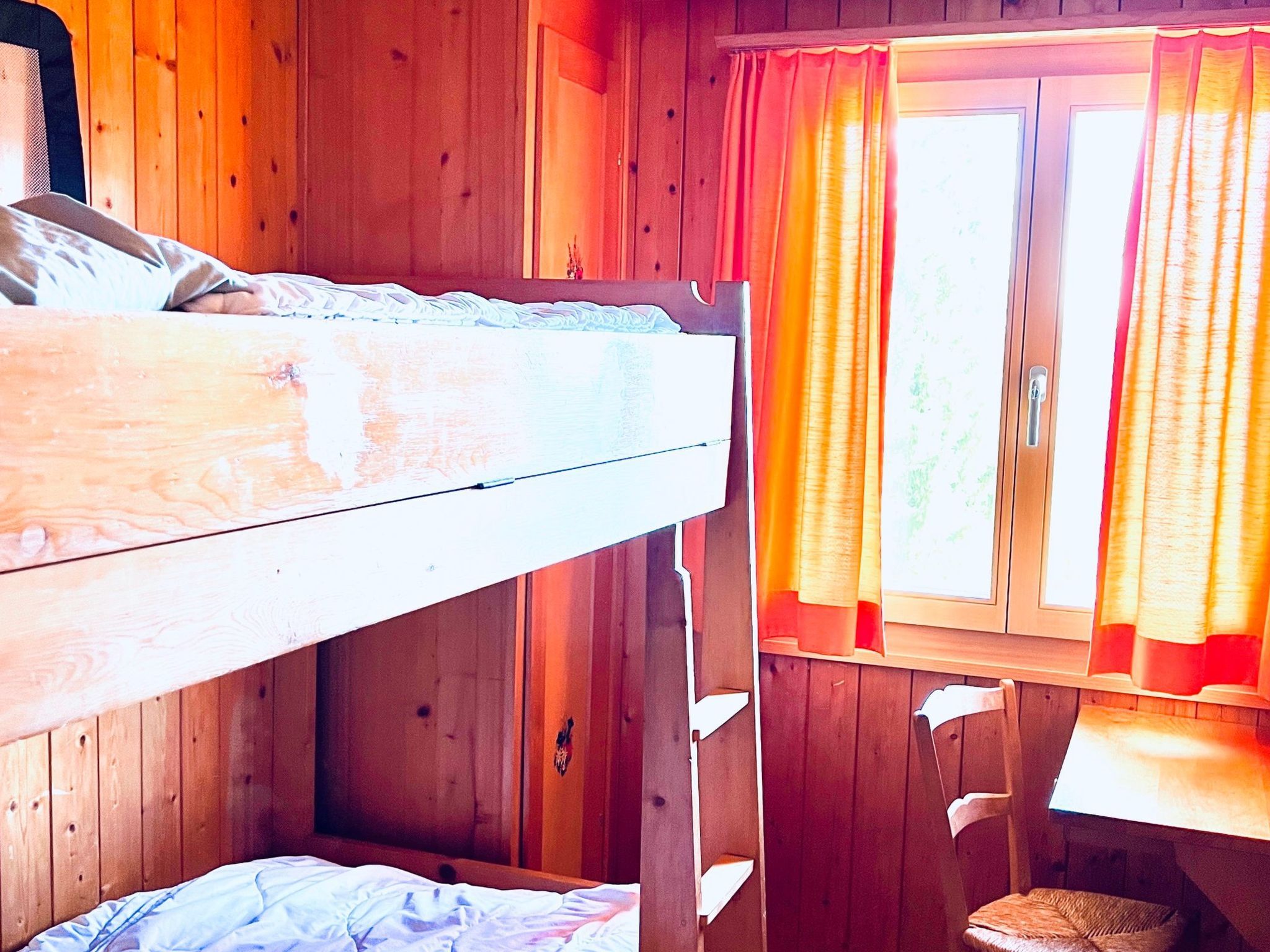 Ein Stockbett in einem Holzraum mit Fenster und Vorhängen.