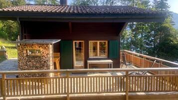 Eine Holzhütte mit einer Holzdiele, einem Kamin aus Stein und Blick auf den umliegenden Wald.
