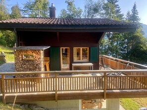 A cabin with a wooden deck, a stone fireplace, and a view of the surrounding forest.