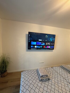 A television mounted on a wall displaying a streaming service interface with various content options. - 2-Bedroom Apartment, Modern (Eggenstein-Leopoldshafen)