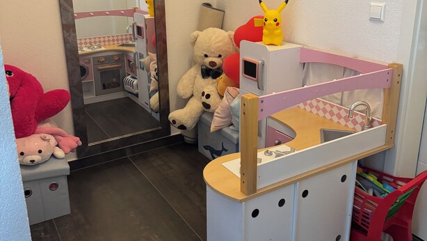 Un'area giochi per bambini con un angolo cottura, uno specchio e un letto con testiera rosa.