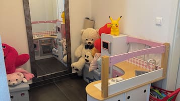 Un espace de jeux pour enfants avec une petite kitchenette, un miroir et un lit doté d’une tête de lit rose.