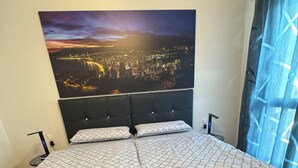 Un letto matrimoniale con vista sulla città, due cuscini e un asciugamano piegato.