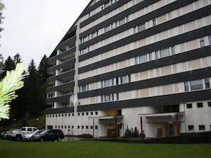 Ein mehrgeschossiges Gebäude mit einer flachen Fassade, großen Fenstern und einem Parkplatz mit Autos.