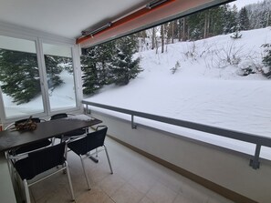 Ein Balkon mit Tisch und Stühlen, mit Blick auf eine verschneite Landschaft mit Bäumen.