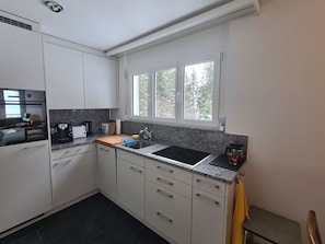 Eine kompakte Küche mit weißen Schränken, einer schwarzen Arbeitsplatte und einem Fenster mit Blick auf Bäume.