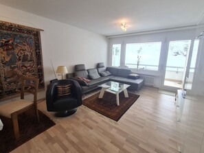 Ein modernes Wohnzimmer mit einem grauen Sofa, einem schwarzen Sessel, einem Glastisch und einem Teppich mit Muster.