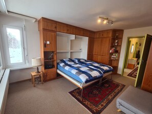 Ein Schlafzimmer mit einem Bett, einem Schreibtisch, einer Lampe und eingebauten Holzsäschränken.