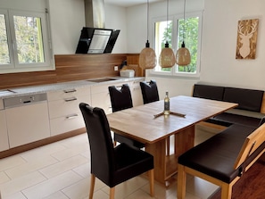 A modern kitchen with a dining area, featuring a wooden table and chairs, a built-in oven, and pendant lights. - Haus Heimetli, (CharmingStay), (Flumserberg Tannenboden), by Interhome (Flumserberg Tannenheim)