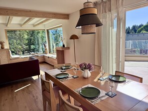 A dining area with a wooden table set for four, large windows, and a hanging lamp. - Haus Heimetli, (CharmingStay), (Flumserberg Tannenboden), by Interhome (Flumserberg Tannenheim)