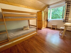 A bunk bed with a pillow, a wooden wardrobe, a small table, and a window with a view of greenery. - Haus Heimetli, (CharmingStay), (Flumserberg Tannenboden), by Interhome (Flumserberg Tannenheim)