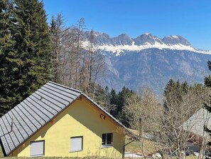 A yellow building with a sloped roof, surrounded by trees and mountains in the background. - Haus Heimetli, (CharmingStay), (Flumserberg Tannenboden), by Interhome (Flumserberg Tannenheim)