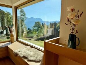 A room with a large window, a wooden bench, a fluffy rug, and a vase with flowers. - Haus Heimetli, (CharmingStay), (Flumserberg Tannenboden), by Interhome (Flumserberg Tannenheim)