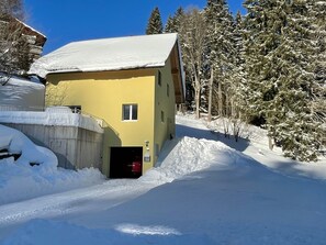 A yellow building with a snow-covered roof, a small entrance, and a staircase leading up to the door. - Haus Heimetli, (CharmingStay), (Flumserberg Tannenboden), by Interhome (Flumserberg Tannenheim)