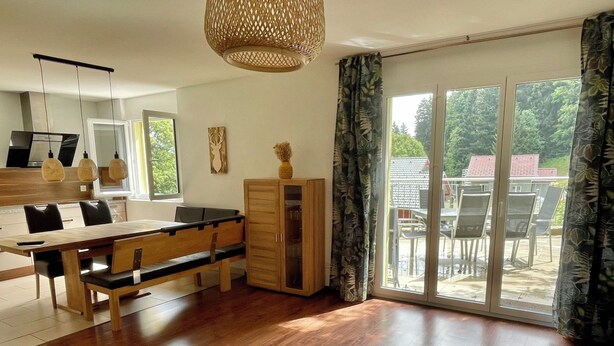 Et moderne køkken med spiseplads, træskabe og en stor skydedør til en udendørs terrasse.