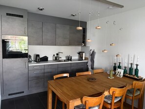 A modern kitchen with grey cabinets, a built-in oven, and a wooden dining table with chairs. - Apartmenthaus Gauenpark (CharmingStay), (Flumserberg Tannenheim), by Interhome (Flumserberg Tannenheim)