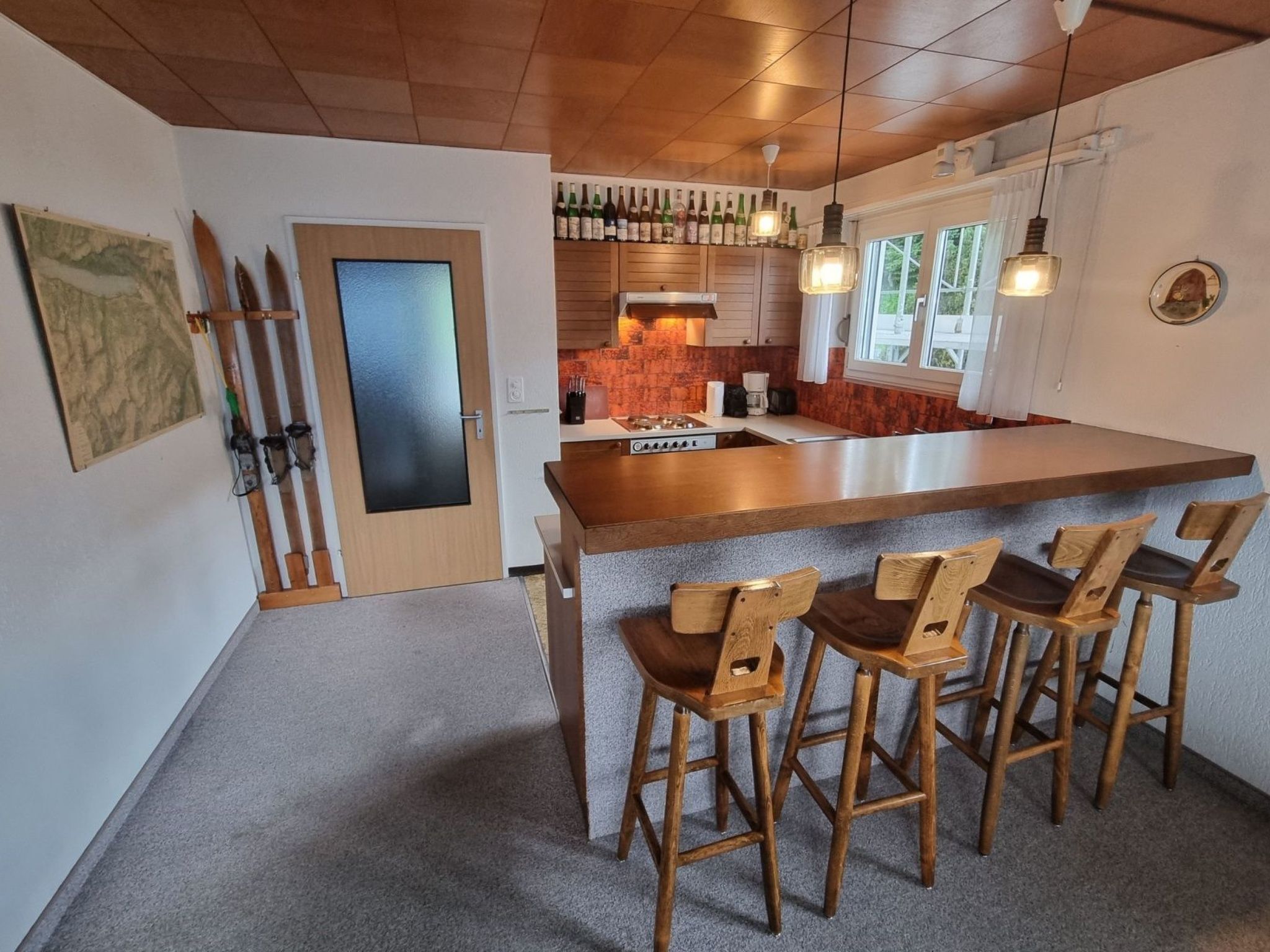A kitchen with a central island, wooden bar stools, and a hanging light fixture.