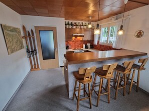 A kitchen with a central island, wooden bar stools, and a hanging light fixture. - Haus Panorama Reeling (CharmingStay), (Flumserberg Tannenheim), by Interhome (Flumserberg Tannenheim)