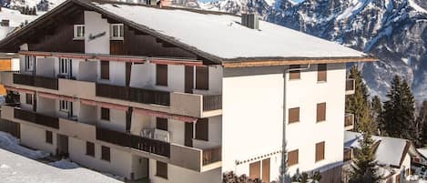 Un edificio de varios pisos con balcones, con una imponente montaña nevada al fondo.