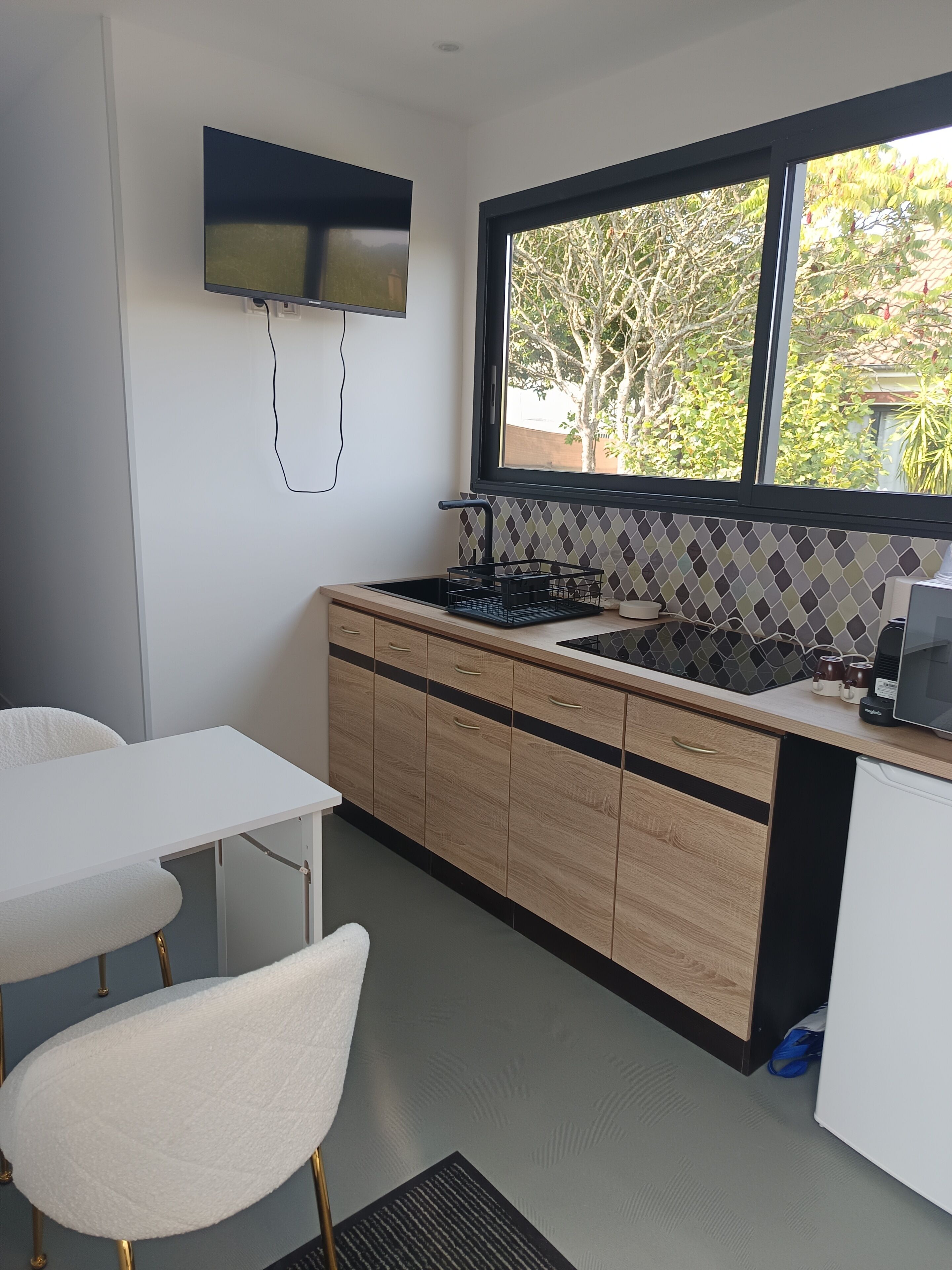 Een moderne keuken met een ingebouwde kookplaat, een raam met uitzicht op bomen, en een witte eettafel met stoelen.