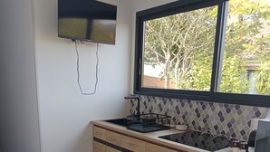 Ett modernt kök med en inbyggd spis, ett fönster med utsikt över träd och ett vitt matbord med stolar.