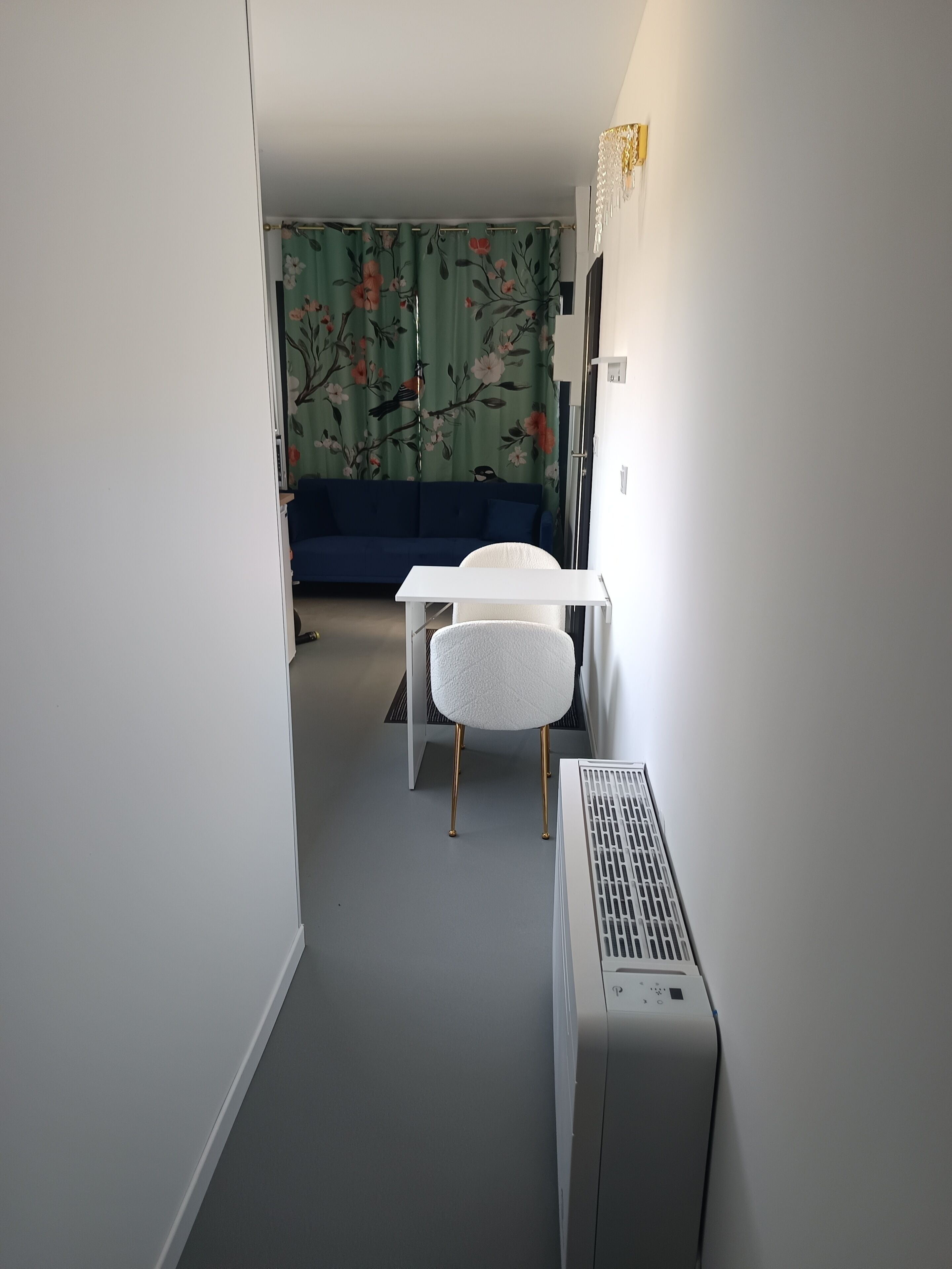 Een smalle gang met een witte radiator, een witte stoel en een blauwe bank op de achtergrond.