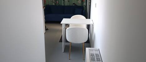 A narrow hallway with a white radiator, a white chair, and a blue sofa in the background.