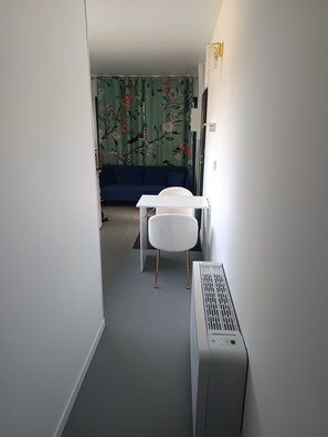 A narrow hallway with a white radiator, a white chair, and a blue sofa in the background.